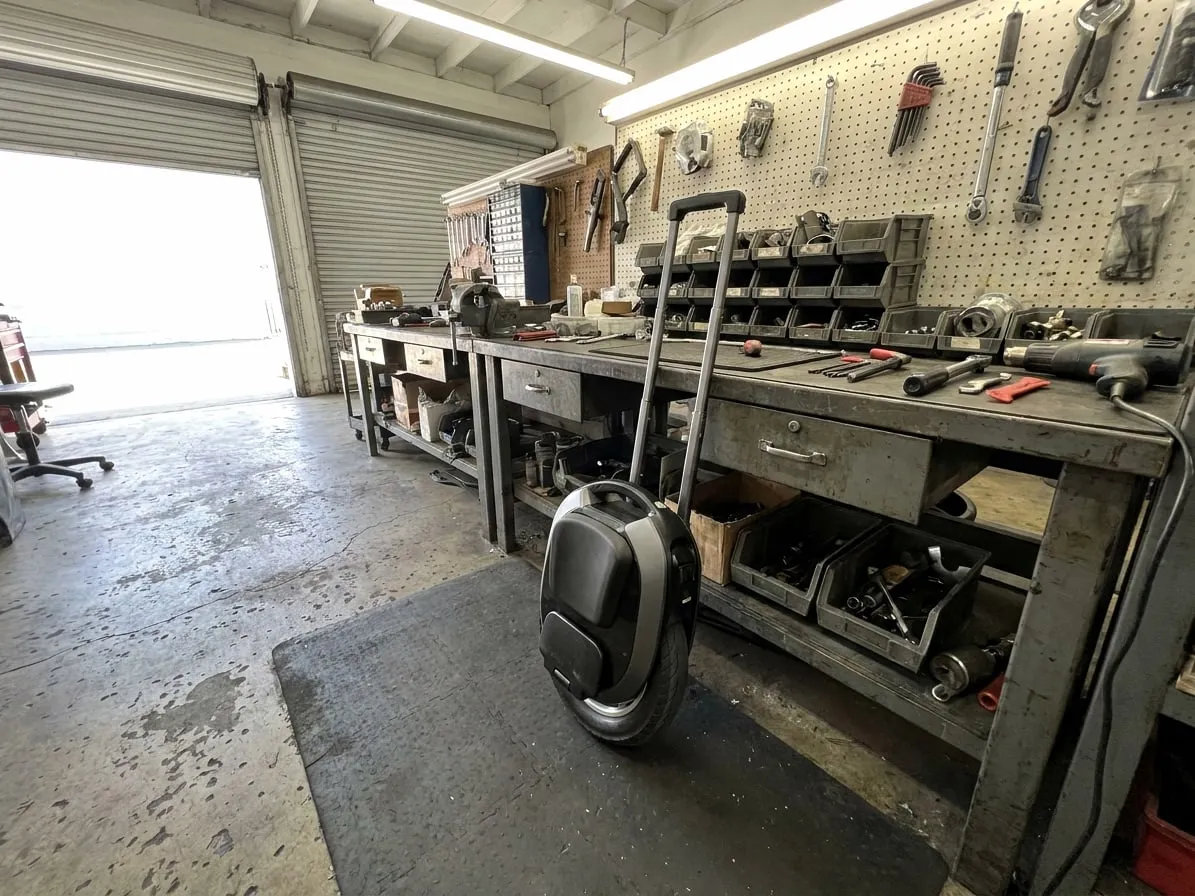 Compact 16-inch commuter electric unicycle with its trolley handle extended in a repair workshop