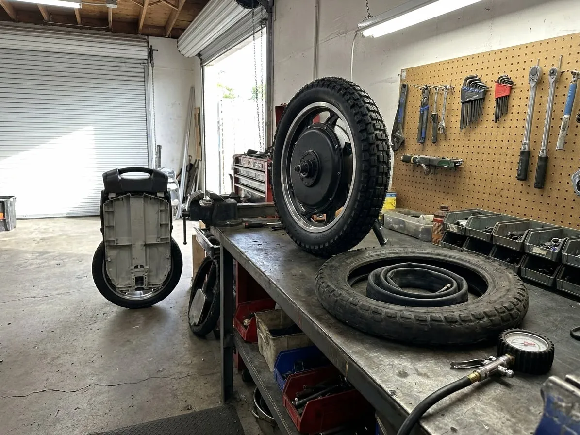 Electric unicycle hub motor with a new knobby tire, the worn old tire and an inner tube beside it on the bench